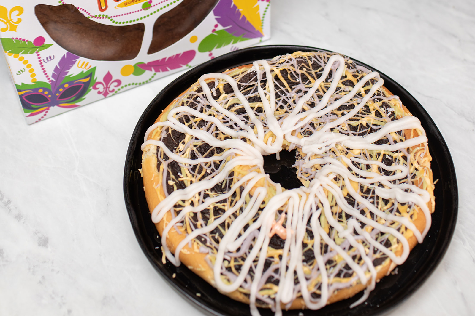 Chocolate king cake with infused icing drizzled atop next to its box